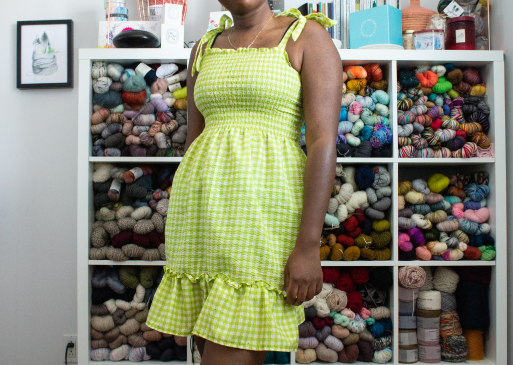 Black woman in lime green dress. Standing in front of a storage unit filled with yarn